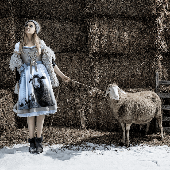 Model trägt St. Malene Dirndl "SLEEP WITH SHEEPS" und hält ein Schaf an einer Leine